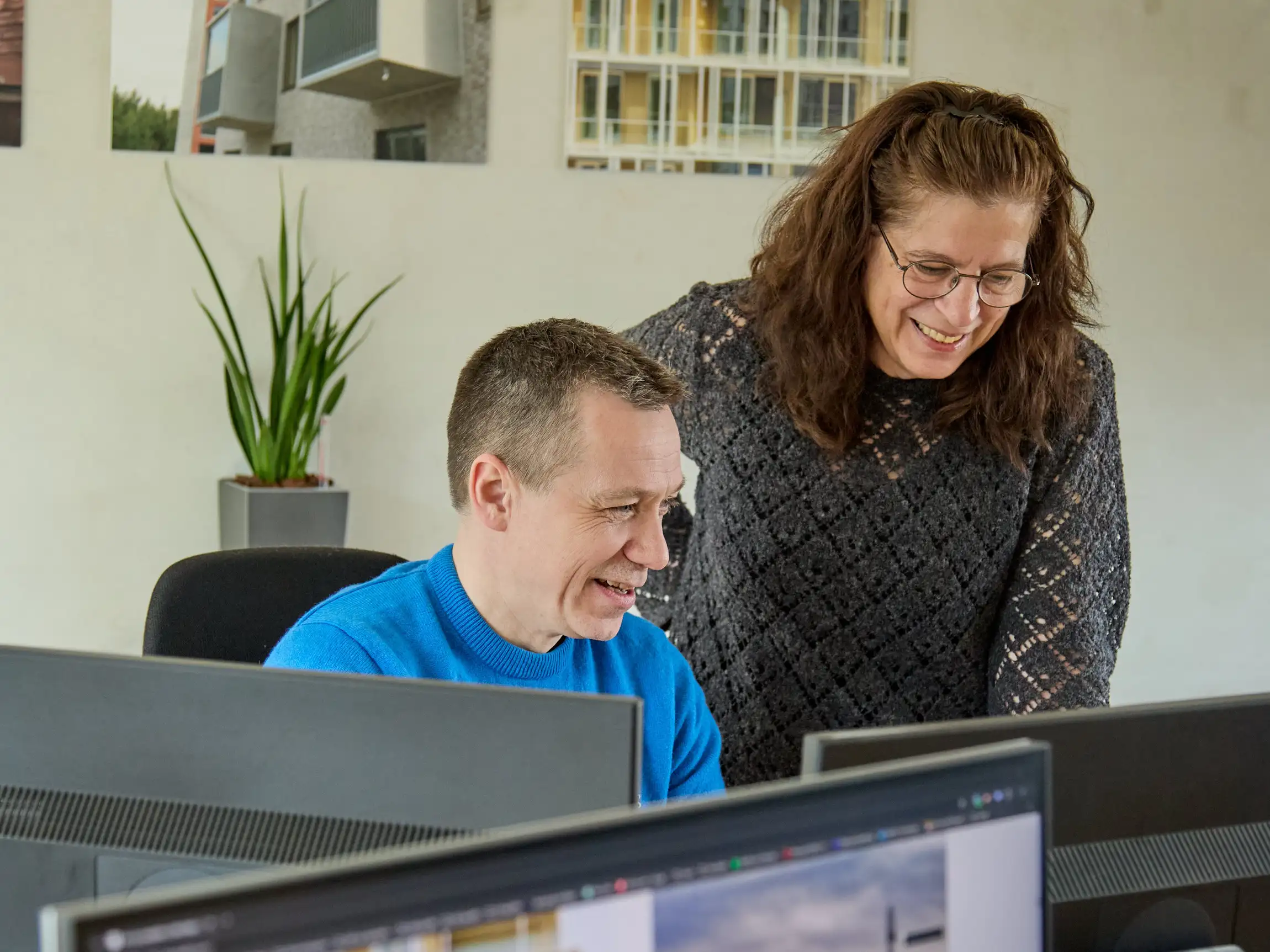 To kontormedarbejdere griner, mens de arbejder sammen